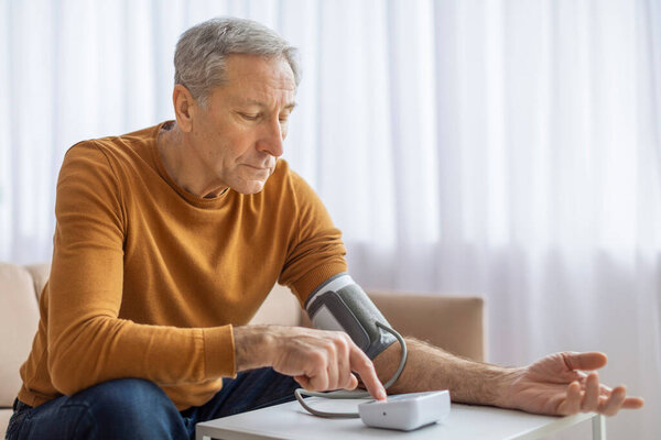 A worried senior man uses a blood pressure monitor at home, suggesting health consciousness, copy space