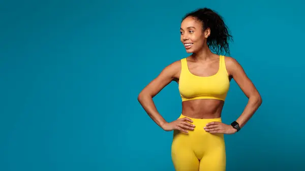 Sebevědomá Atletická Afroameričanka Pózuje Žlutém Aktivním Oblečení Pulzujícím Modrém Pozadí — Stock fotografie