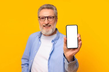 Harika bir uygulama. Mutlu gülümseyen son sınıf öğrencisi akıllı telefonunu boş ekranda gösteriyor, mobil uygulama tanıtımı için model öneriyor, stüdyo sarı arka planda boş cihaz dokunmatik ekranı ile poz veriyor.