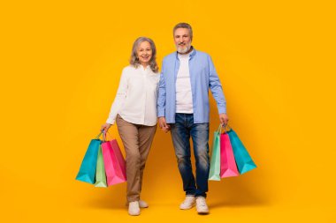 Kara Cuma. Neşeli yaşlı çift sarı stüdyo arkaplanına karşı alışveriş torbaları tutuyor, el ele yürüyor ve içinde alışveriş paketleri taşıyor. Mevsimlik anlaşmalar, olgun tüketim