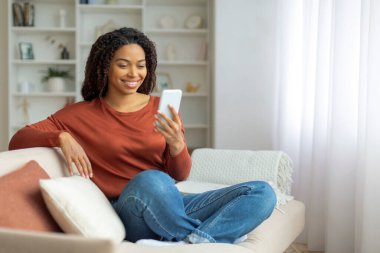 Kapalı bir koltukta oturan siyahi kadın, Afrika kökenli Amerikalı bir kadın cep telefonu kullanıyor, internetten mesajlaşıyor ya da internette arama yapıyor.