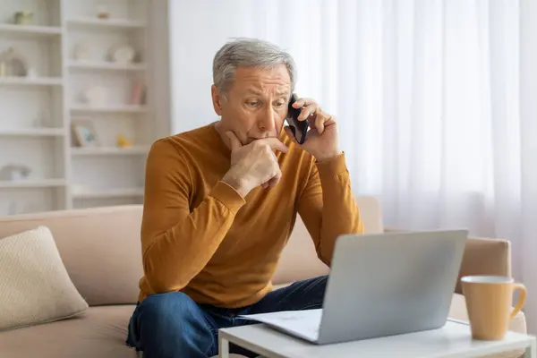 Starszy Pan Koncentrujący Się Rozmowie Telefonicznej Laptopem Otwartym Przed Nim — Zdjęcie stockowe