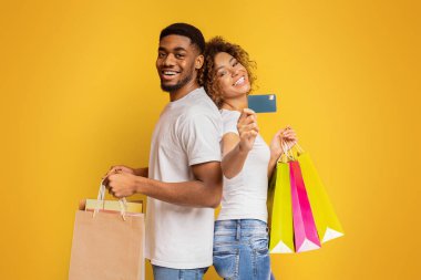 Bankamız alışveriş torbaları ve kredi kartı, turuncu arka plan ile mutlu bin yıllık bir Afrikalı-Amerikalı çift seviyoruz