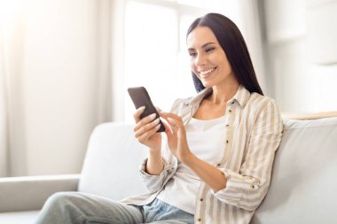 Sakin ve sakin bir kadın koltukta oturmuş akıllı telefonuyla etrafı kolaçan ediyor.