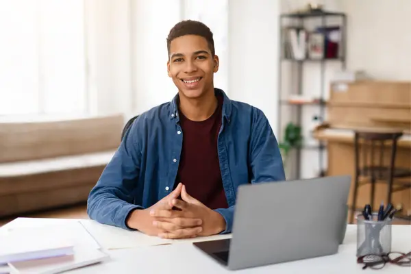 快乐的非洲裔美国少年坐在办公桌前 拿着笔记本电脑 自信地对着相机笑 对学习或远程工作表现出准备和乐观 — 图库照片
