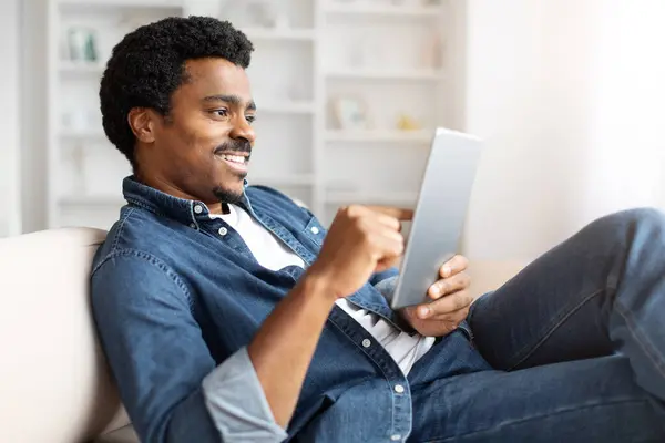 Hombre Negro Sentado Sofá Interactuando Con Tableta Digital Sus Manos —  Fotos de Stock