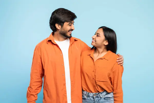 インドの男性と女性はカジュアルなオレンジ色のシャツで一緒に立って 固体青色の背景に対して暖かいディスプレイを作り 顔がぼやけています — ストック写真