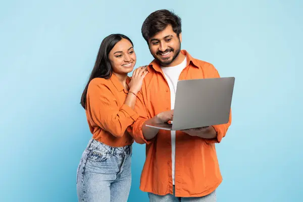 コラボレーションしながら笑顔のオレンジ色の服装のインドのカップル ラップトップの画面を見る 現代の仕事の概念 — ストック写真