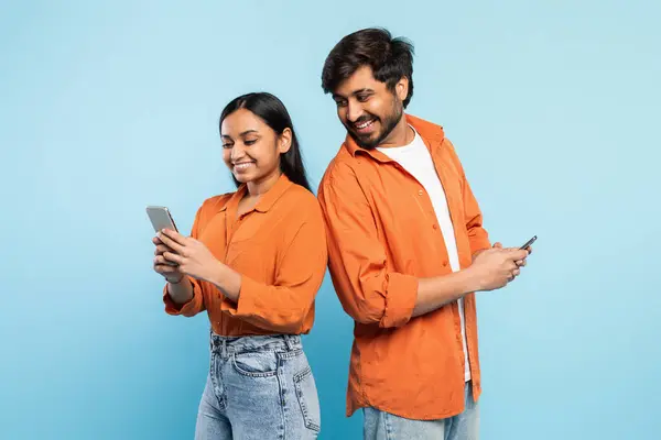 彼らの携帯電話を使用してカジュアルな若いインドのカップルは 青い背景を持つ個人的なデジタル世界に魅了 — ストック写真