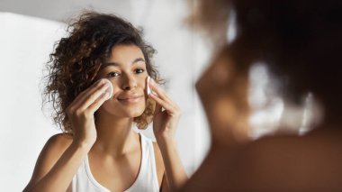 Güzel Afro-Amerikan kız banyo aynaya bakarak pamuklu ped ile yüz temizliği. Günlük makyaj çıkarmadan kavramı