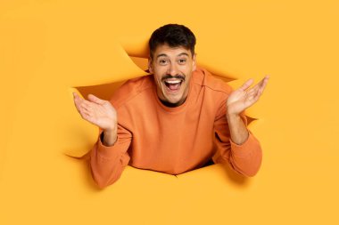 Surprised funny man popping through a hole in a yellow backdrop, with a playful and excited expression clipart
