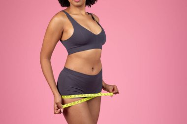 Fit young african american woman self-measuring her waist with a tape, indicating health, wellness, and fitness goals clipart