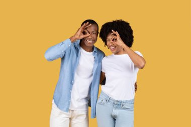 Neşeli bir Afro-Amerikan çifti, sarı arka planda ellerini kullanarak neşeli bakışlar atıyor.