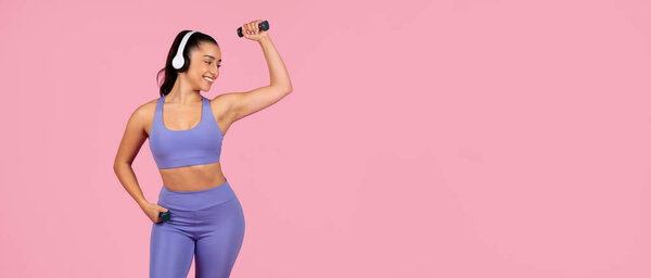 A fit woman in a sports bra and leggings listens to music, dancing and enjoying herself on a pink background