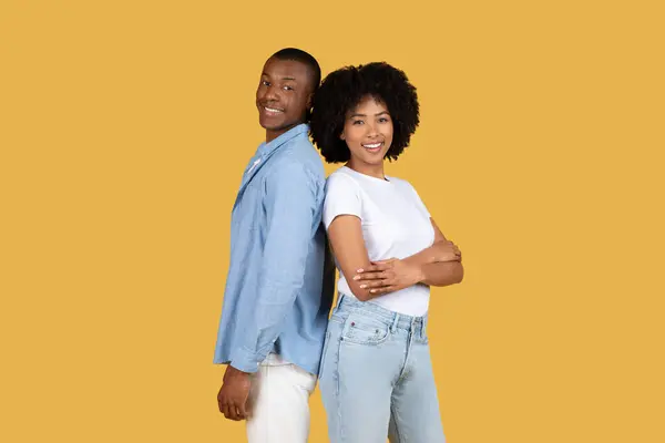2人の笑顔の若いアフリカ系アメリカ人のカップルは 自信と満足を除いて 黄色の背景を快適にポーズバックに戻って後ろに立ちます — ストック写真