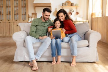 Neşeli bir aile, kanepede birlikte dijital tablet kullanmaktan keyif alır, sıcaklığı ve yakınlığı gösterir.
