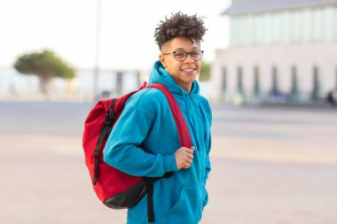 Gözlüklü, kırmızı sırt çantalı, mavi kapüşonlu neşeli, genç bir öğrenci.