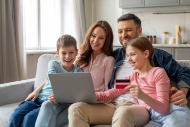 A family of four is engaged in online shopping as one of the children holds a credit card while looking at a laptop clipart