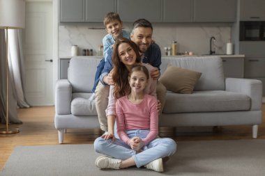İki çocuklu bir aile yerde oturur, arka planda kanepe olan neşeli bir merdiven yapar.