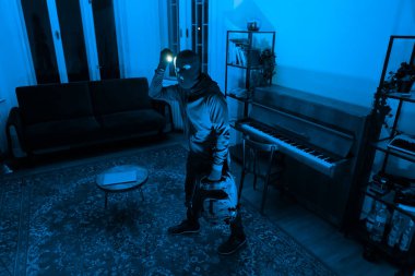 Elinde parlak bir ışıkla, bu siluetli figür, mavi tonlarda gizemli bir karanlık boşlukta arama yapıyor.