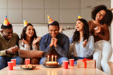 Bir grup neşeli çok ırklı arkadaş bir evde toplanmış pasta ve mumlarla doğum günü kutlamalarının tadını çıkarıyorlardı.