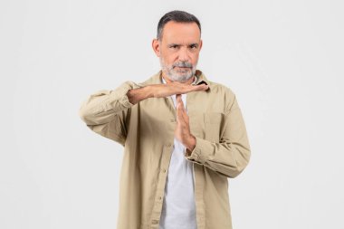 A mature man with a beard in casual attire making a time out or pause gesture with his hands against a white background clipart