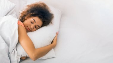 Rahat Afro-Amerikalı kadın yatakta uyuyor ve evde yastığa sarılıyor.