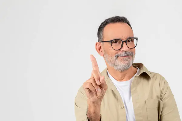 stock image A confident elderly man with glasses pointing upwards with one finger and smiling, set against a white background