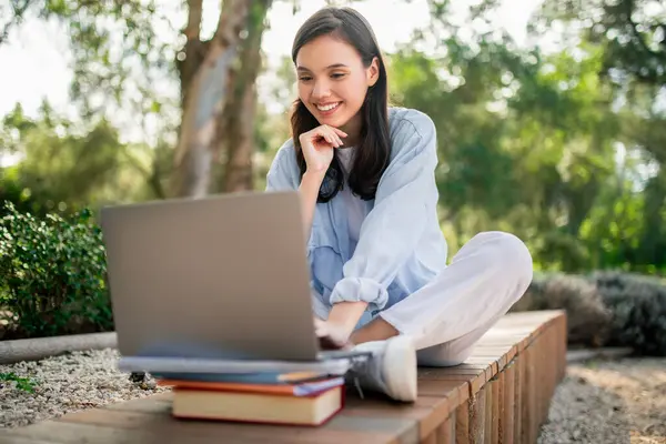 A focused woman studies with a laptop and books, blending outdoor relaxation with productivity and learning