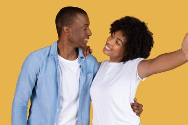 A young African American couple poses playfully as they take a selfie, displaying a moment of joy and connection clipart