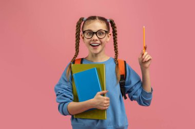 Kalem ve parlak pembe arkaplanlı renkli defterlerle gülümseyen liseli kızın yaratıcı bir fikri var.