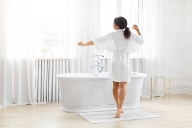 Afro-Amerikan kadın, saadeti yakalamak için el değmemiş, beyaz bir banyoda kollarını banyodan açıyor.