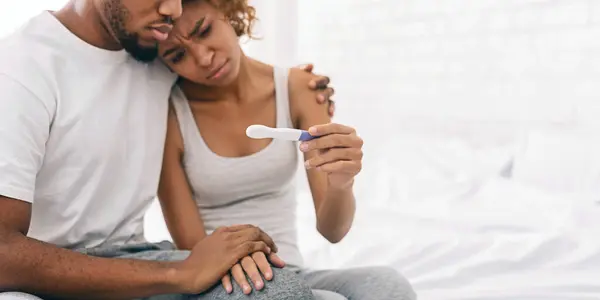 Infertility problem. Black couple sitting with negative pregnancy test result, free space