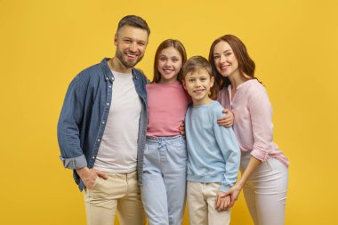 Mutlu bir aile, iki çocuk bir arada, sarı bir arka plana karşı aile birliği sergiliyorlar.