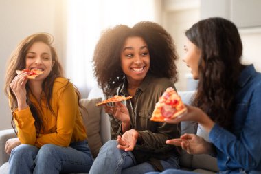 Sıradan bir yemeğin tadını çıkaran, üç çok ırklı kadın pizza yiyor ve evlerinde sıcak ve dost canlısı bir ortamda sohbet ediyorlar.