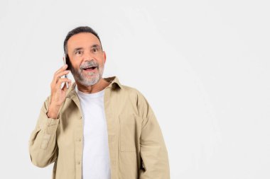 Gri sakallı neşeli yaşlı bir adam cep telefonuyla bir sohbete dalıyor, mutluluk ve şaşkınlık ifade ediyor.