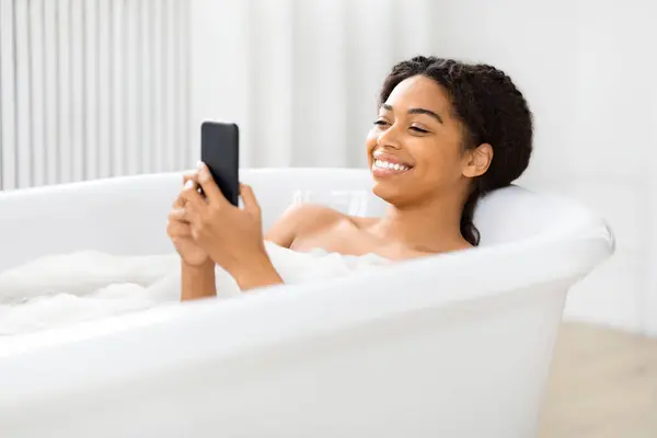 Rahatlamış Bir Afrikalı Amerikalı Kadın Duş Alırken Akıllı Telefonuyla Meşgul — Stok fotoğraf