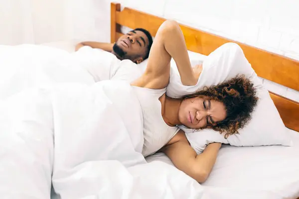 Stop snoring African-american woman covering ears with pillow, hiding from her husband noisy breathing, panorama