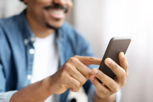 一个快乐的黑人与他的智能手机互动 他的内容使他的脸上带着微笑 特写镜头 — 图库照片