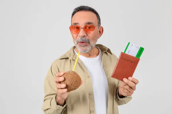 戴着时髦太阳镜的快乐老人拿着护照和登机牌 一边喝着椰子 暗示要去热带度假 — 图库照片
