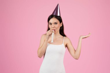 Avrupalı bir bayan parti şapkası ve ıslıkla kutluyor, kapsüllü kuşak z yaz eğlencesi, pembe bir arka planda izole edilmiş
