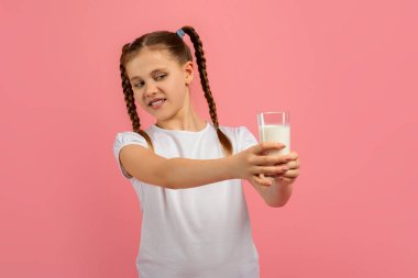 Disgust young girl gazes at a glass of milk she holding, against a pink background, dont like dairy products clipart