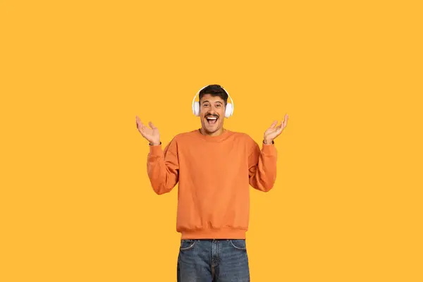 stock image Excited young man with headphones on his head expressing joy and surprise on an orange background, copy space