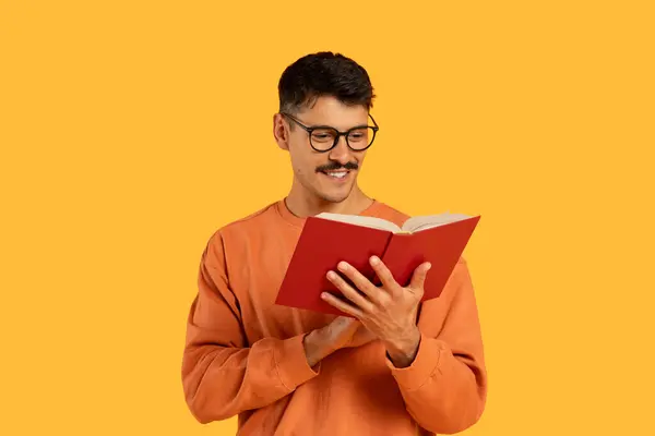 Mężczyzna Luźnej Odzieży Okularach Głęboko Pochłonięty Czytaniem Czerwonej Książki Pomarańczowym — Zdjęcie stockowe