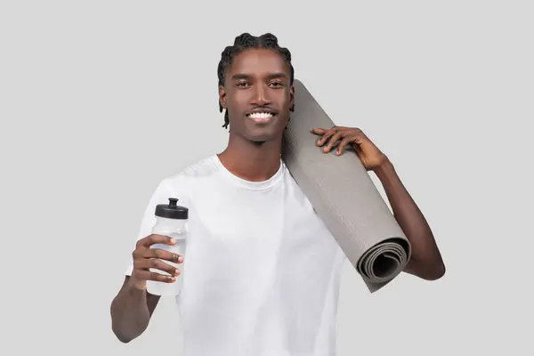 自信を持った若いアフリカ系アメリカ人男性 肩にヨガマットと白い背景のスポーツボトル — ストック写真