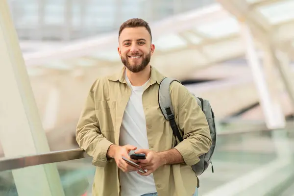 空港に立っている間パスポートとスマートフォンを保持している陽気な若者 幸せなミレニアル世代男性は 今後の旅行に興奮し スペースをコピー — ストック写真