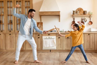 Baba ve kızı, iç açıcı bir evde tahta kaşıklarla kılıç dövüşü yapıyormuş gibi davranıyorlar.