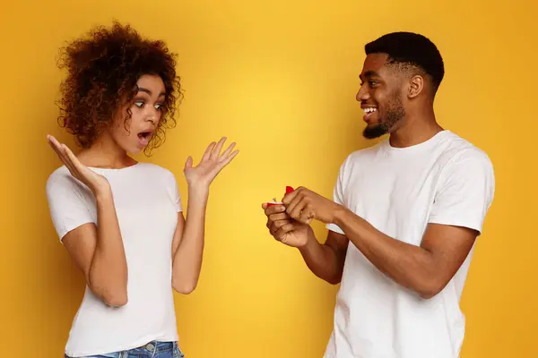 令人惊讶的提议 震惊的非洲裔美国女人看着她的男朋友与订婚戒指 橙色背景 — 图库照片