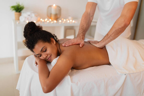 Relaxed African American woman enjoys a professional back massage from a man therapist at a modern spa