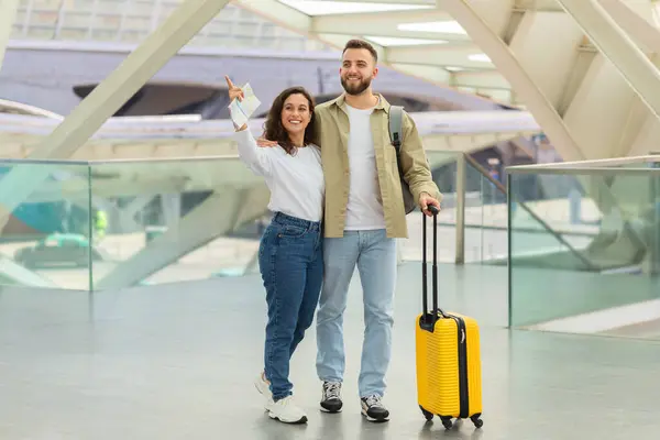 Cheerful Couple Standing Luggage Airport Terminal Pointing Away Smiling Man — Stock Photo, Image